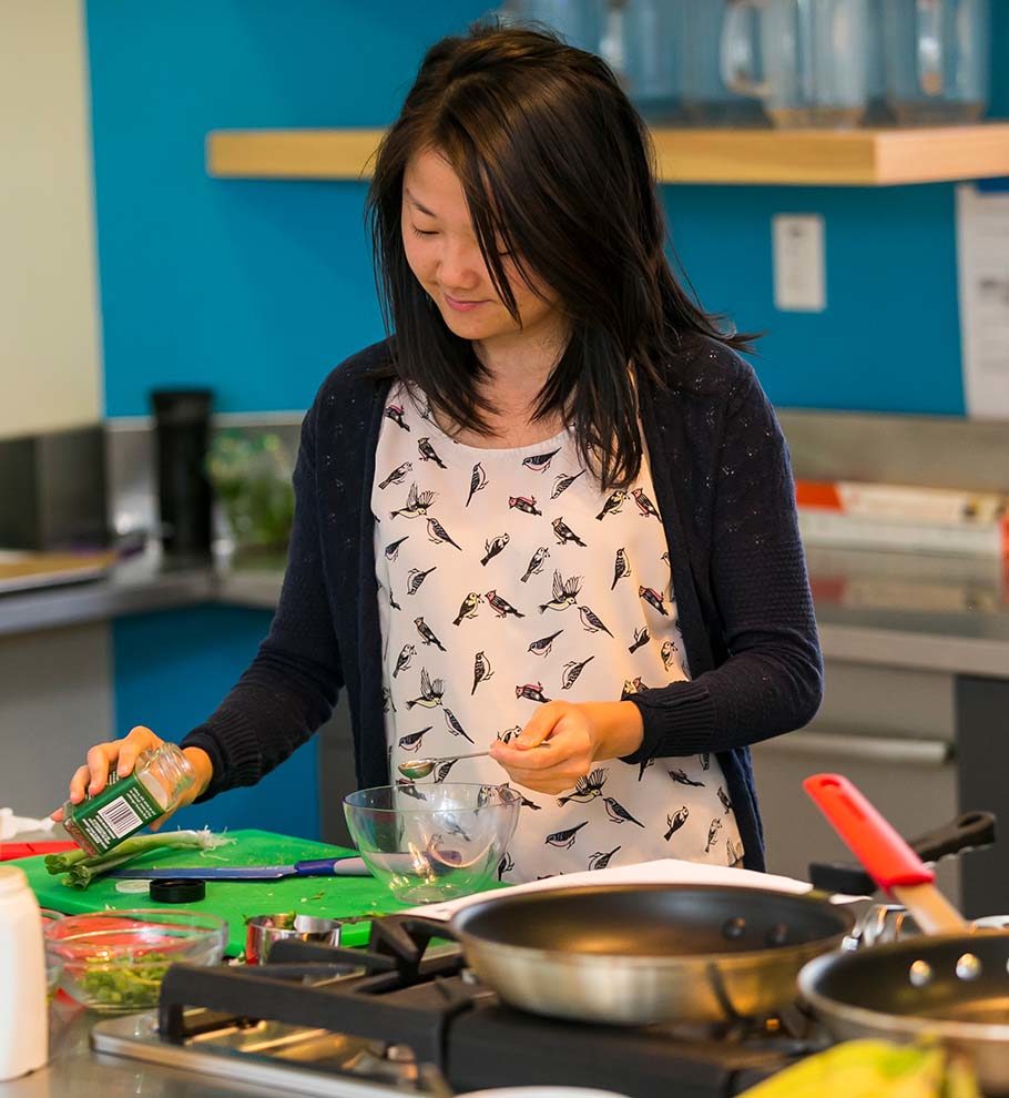 woman with long black hair wearing an apron with small black birds ads spice to a bowl