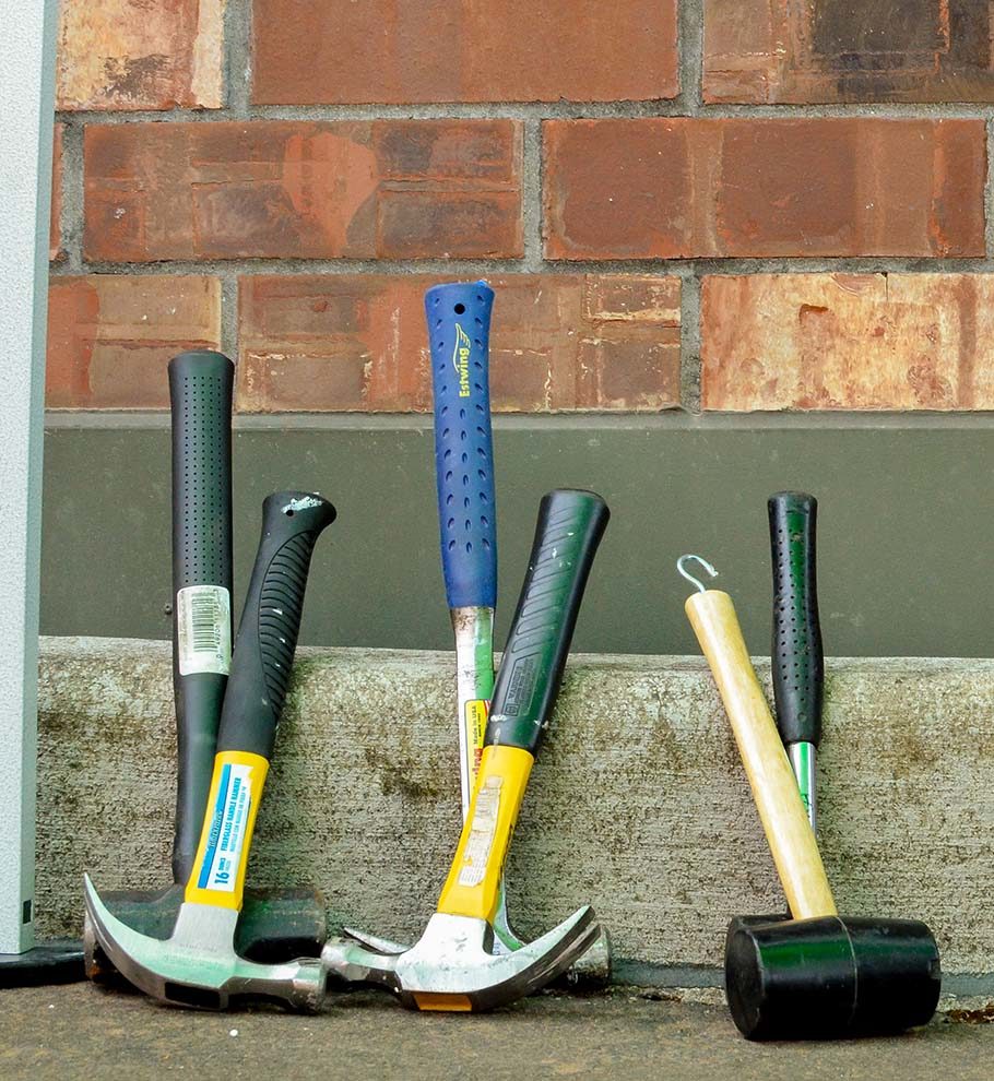 a collection of hammers and mallets resting against a curb