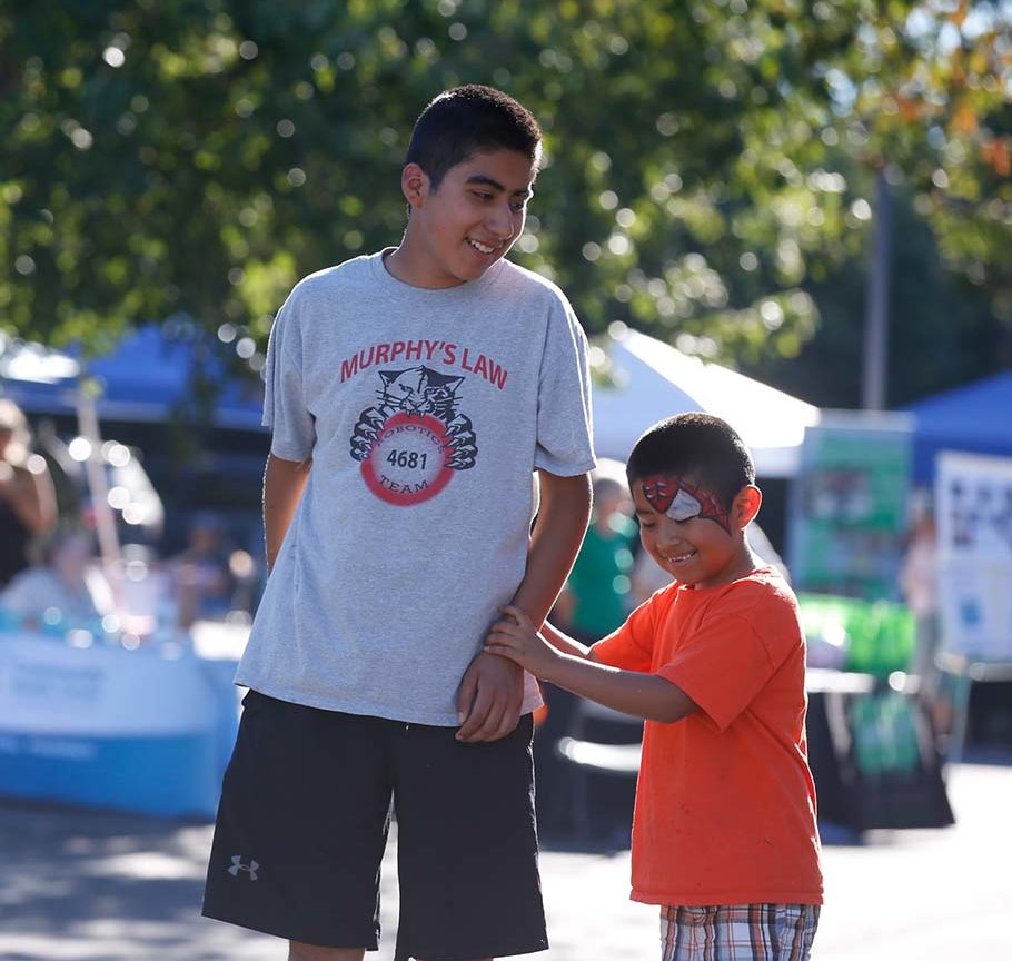 Teen boy smiles at younger brother who is holding his hand and laughing