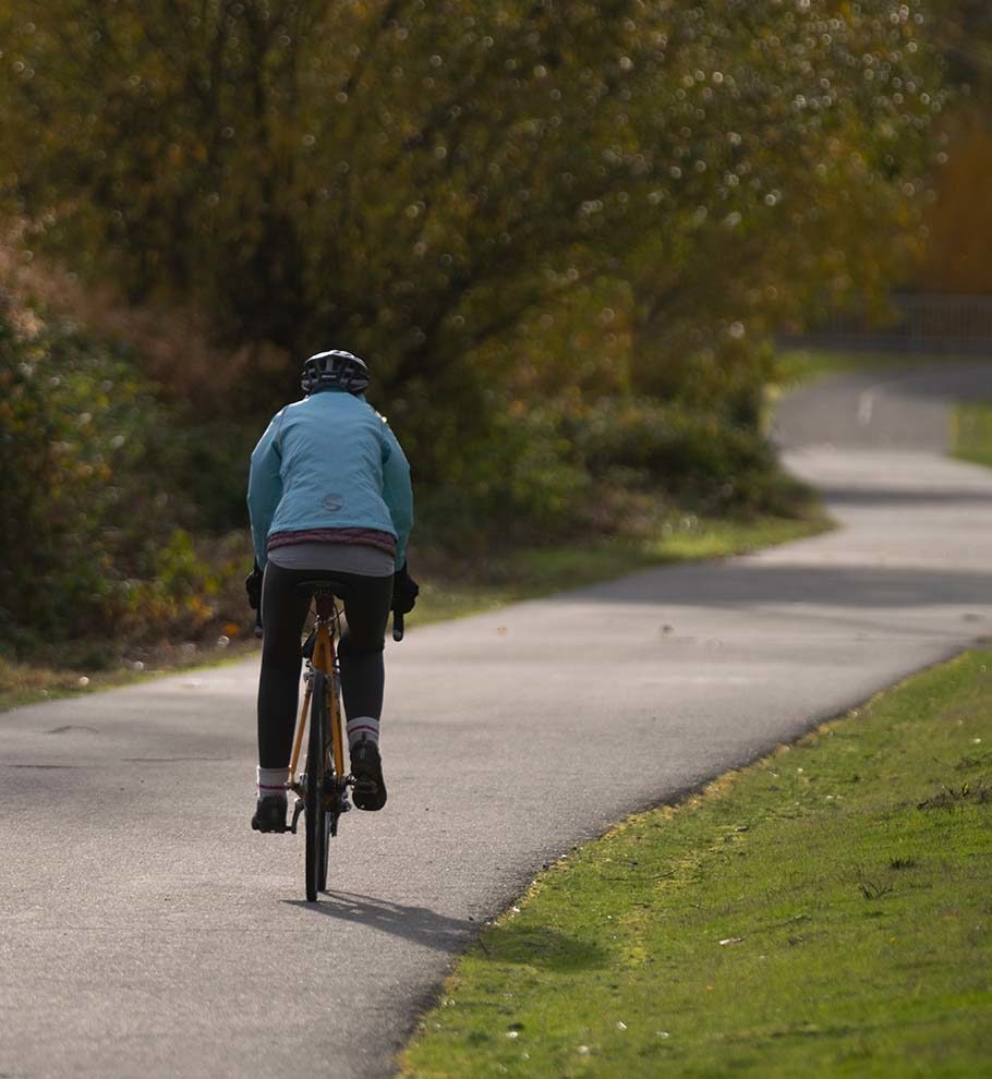 person in blue winter coat riding bike on path through park